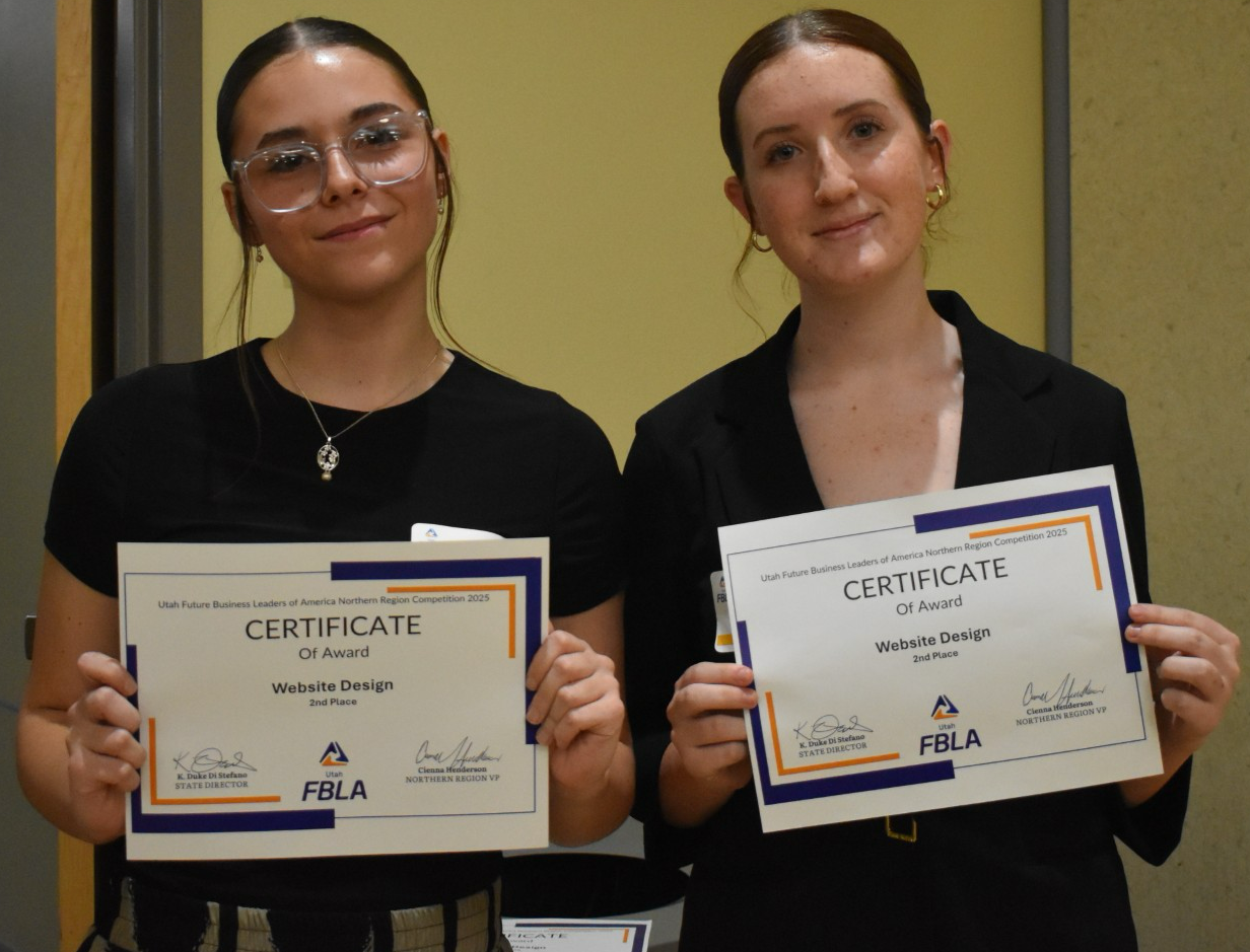 Two young women stand side-by-side, each proudly holding up a certificate.